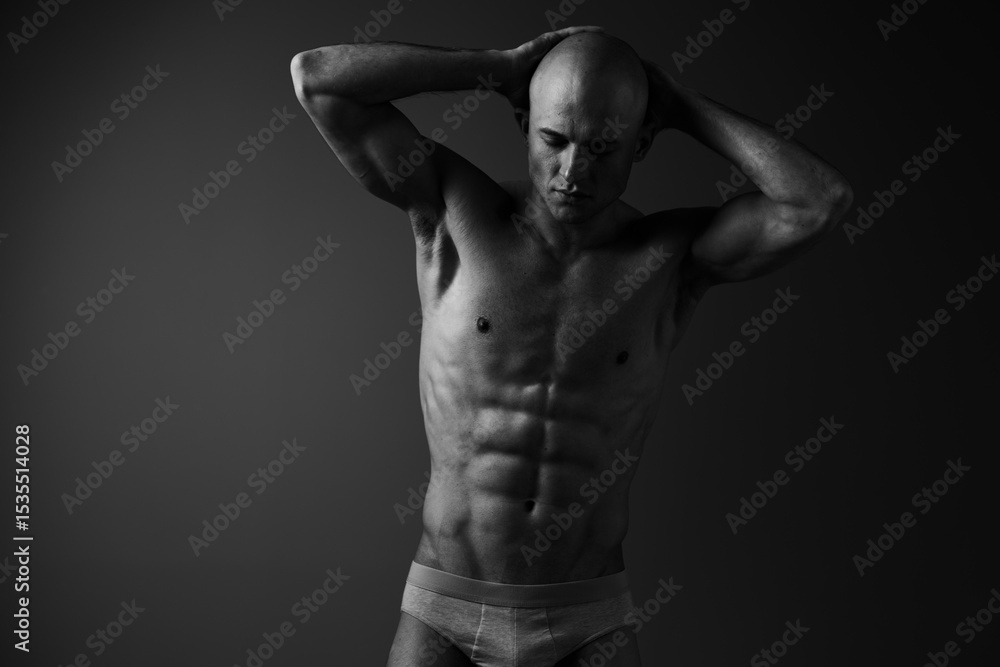 Fototapeta premium Black and white image of a muscular man posing confidently with his hands behind his head, showcasing his athletic physique and expression of strength and focus.