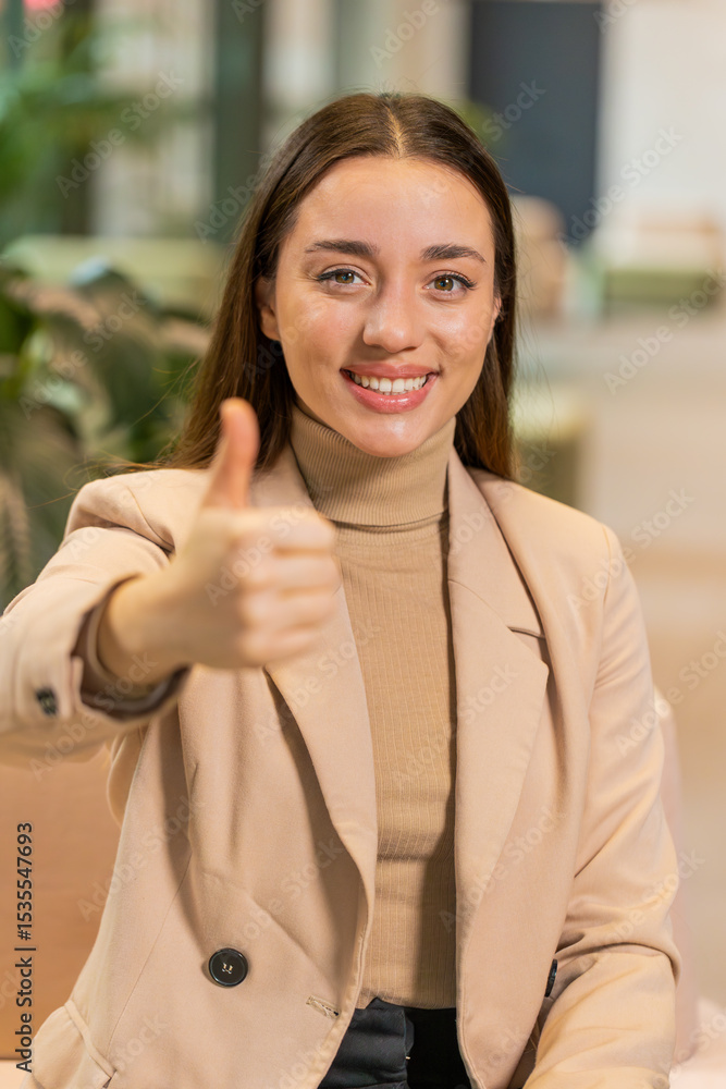 Happy overjoyed Caucasian businesswoman excited winner celebrate victory success concept looking at camera showing thumbs up sitting in office lobby. Portrait of girl employee in formals in hotel hall Happy overjoyed Caucasian businesswoman excited winner celebrate victory success concept looking at camera showing thumbs up sitting in office lobby. Portrait of girl employee in formals in hotel hall