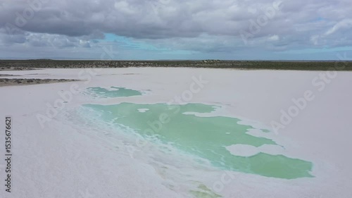 Turquoise water and salt flat surface, reflecting cloudy sky and revealing environmental transformation under expansive landscape. Saline pond in Guerrero Negro, Baja California, Mexico