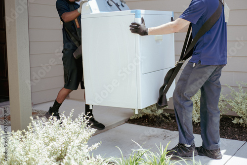 New house door entrance with two professional mover uses lifting straps carry large dryer household appliance, wearing gloves workwear, home services, appliance delivery, moving concept, Texas