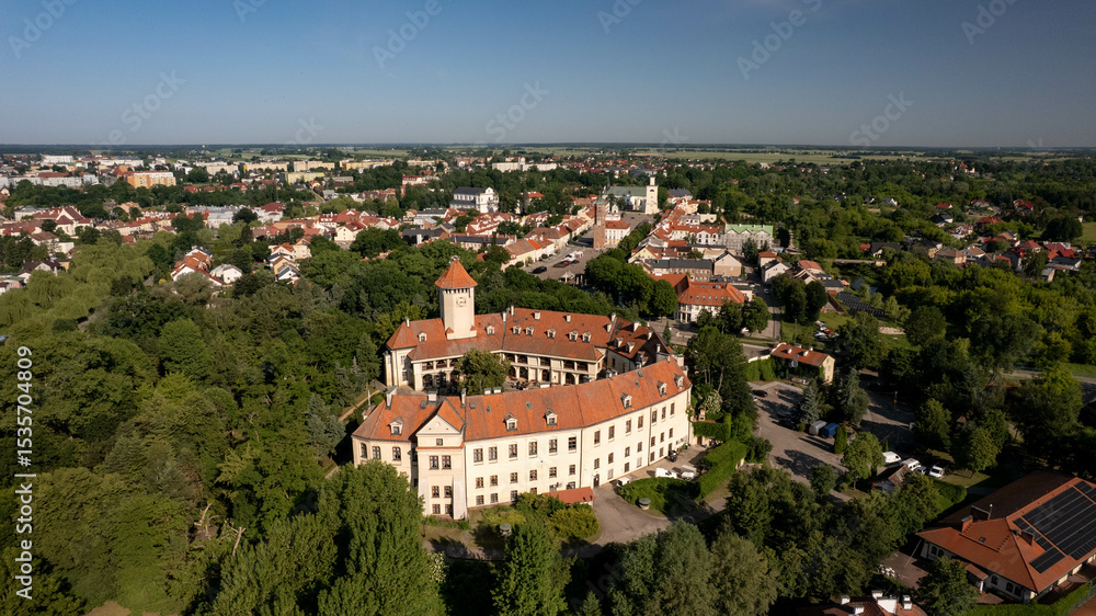Fototapeta premium Aerial view of a charming Polish town with red-roof houses, a central square, and a historic castle surrounded by green trees. Beautiful European architecture on a sunny summer day.