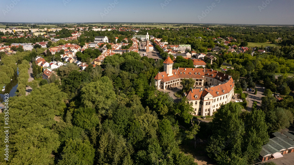 Obraz premium Aerial view of a charming Polish town with red-roof houses, a central square, and a historic castle surrounded by green trees. Beautiful European architecture on a sunny summer day.