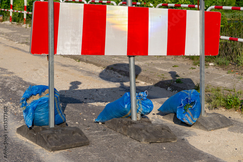 Fotografie temporary roadwork barrier with red and white warning stripes, secured with blue sandbags