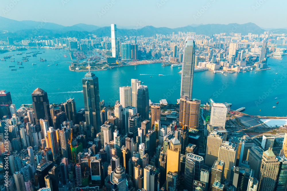 Fototapeta premium Numerous high-rise buildings dominate the urban landscape of Hong Kong. The blue waters of the harbor are dotted with boats and vessels, while the distant mountains provide a scenic backdrop