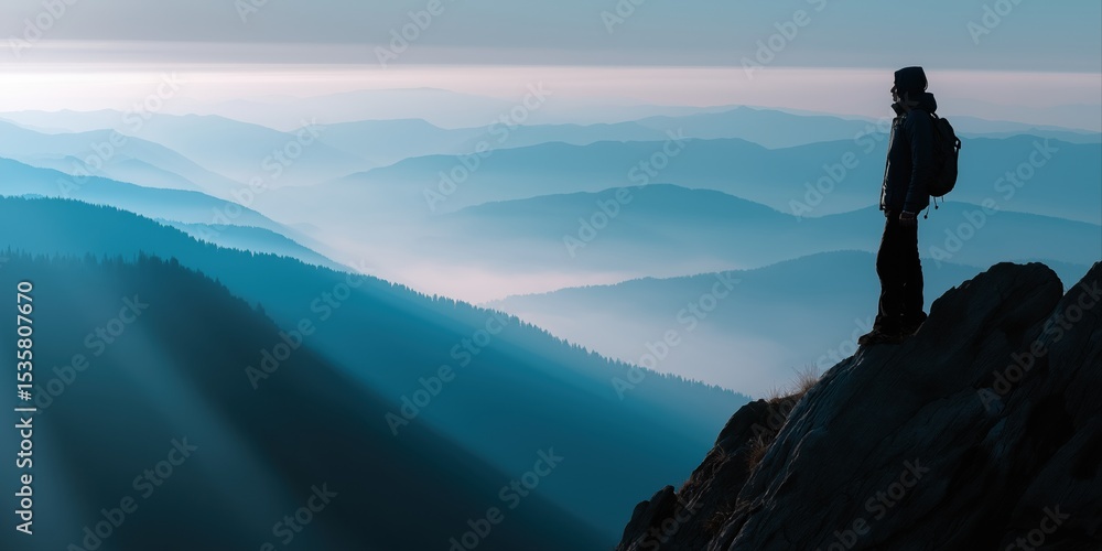 Fototapeta premium A man stands on a mountain top with a backpack. The sky is blue and the mountains are in the background