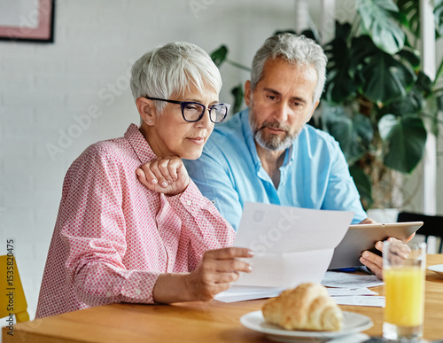 Senior couple checking bills and calculating expenses using a tablet at home, debt taxes and home budget concept, business meeting in office, businessman and businesswoman