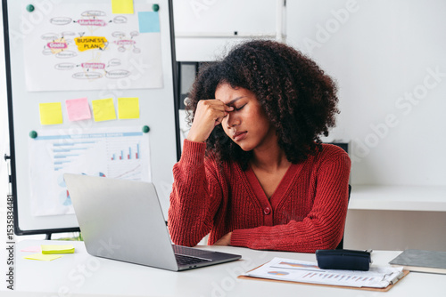 A woman is sitting at a desk with a laptop and a stack of papers