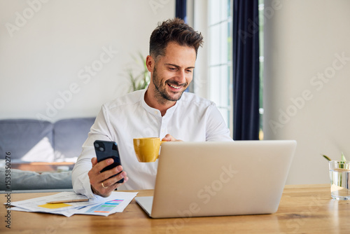 Man using laptop and mobile phone while working from home