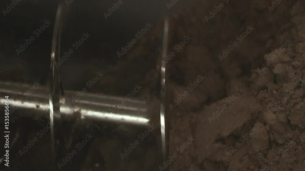 Detailed close up revealing industrial auger rotating and transporting brown malt grains inside modern brewery manufacturing environment, highlighting grain processing mechanism Detailed close up revealing industrial auger rotating and transporting brown malt grains inside modern brewery manufacturing environment, highlighting grain processing mechanism