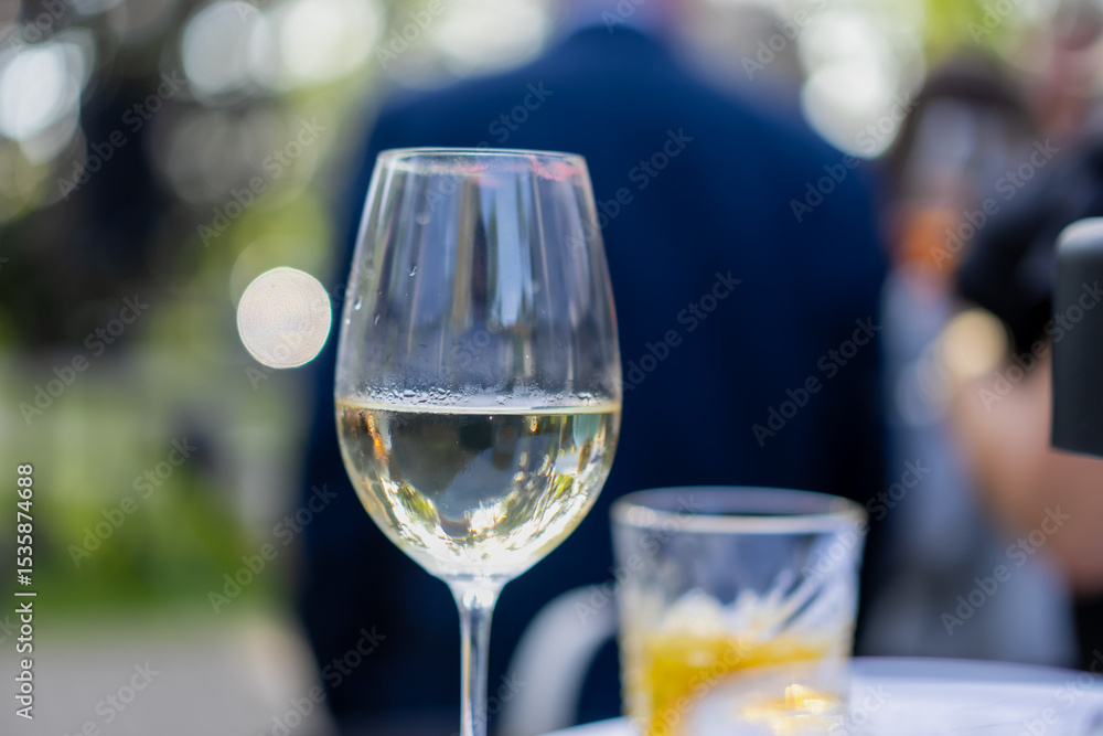 close up of white wine glass and cocktail on table at elegant outdoor event or wedding reception with guests in background, celebratory atmosphere with drinks, social gathering, summer party scene close up of white wine glass and cocktail on table at elegant outdoor event or wedding reception with guests in background, celebratory atmosphere with drinks, social gathering, summer party scene