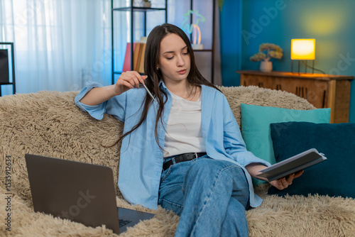 Φωτογραφία Young tired woman at home exhaustedly working on laptop and notebook after remote studying session, deeply exhaling tiredly