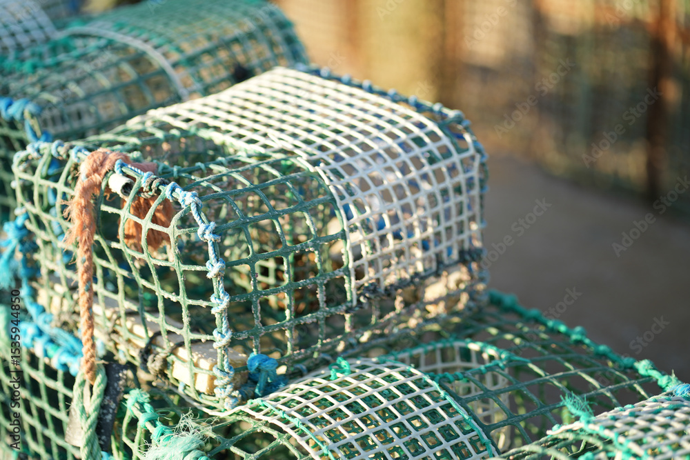 Obraz premium Crab traps are neatly stacked, showcasing their mesh structure and vibrant colors. The early morning sunlight highlights the traps placed on a coastal fishing site, ready for use.