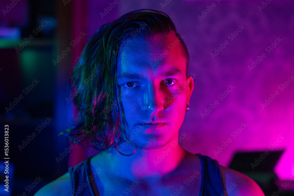 A young caucasian male with long hair and earrings is captured in moody neon lighting, highlighting contemporary urban style. vibrant pink and blue tones create a dramatic effect. A young caucasian male with long hair and earrings is captured in moody neon lighting, highlighting contemporary urban style. vibrant pink and blue tones create a dramatic effect.
