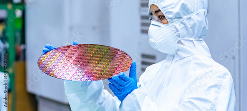 Fotografie A female worker in protective clothing inspects silicon wafers in a semiconducto