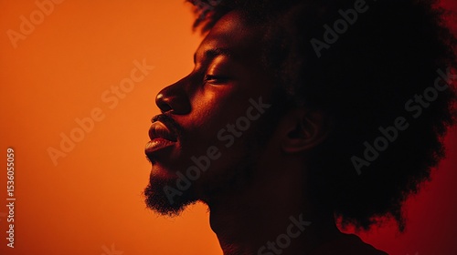A close up shot of a man with afro hair profile side view against warm orange background