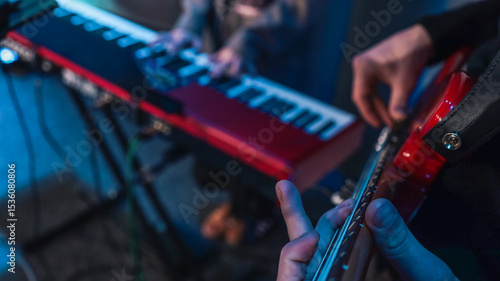 Close-up of hands playing electronic keyboard during live music performance with blurred bassist in background under blue lighting