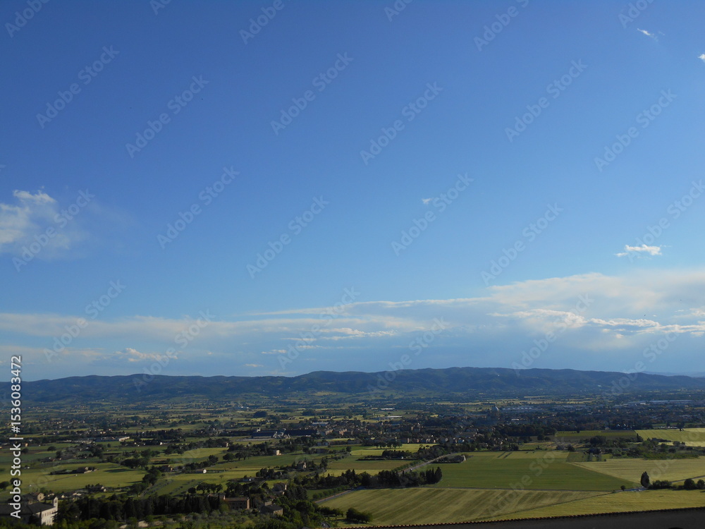Fototapeta premium イタリア・アッシジの田園風景と遠くに続く山並み｜青空と広大な大地が広がる美しい風景 Scenic countryside view of Assisi, Italy｜Wide open fields and distant hills under a clear blue sky