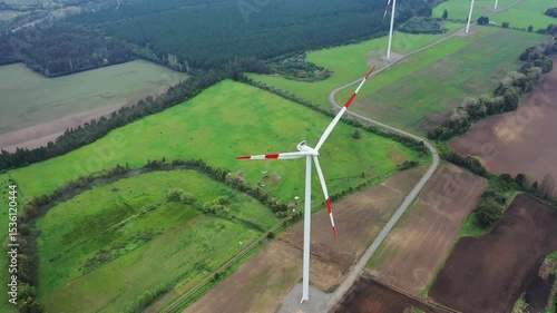 Wind turbine stands tall over lush green fields in rural area during daytime