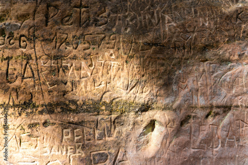 Close-up of an ancient sandstone wall covered in engraved names and carvings, showcasing human marks left over generations.