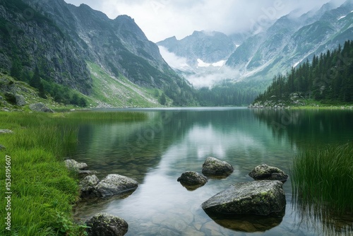 Fototapeta Naklejka Na Ścianę i Meble -  Serene mountain lake reflecting majestic peaks under a misty sky offers breathtaking nature scenery