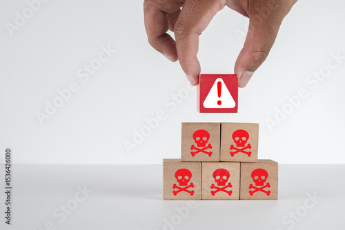 Фотография Hand placing a red warning triangle block on top of skull and crossbones icons on white background