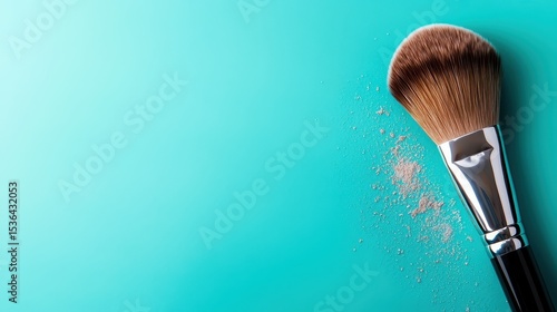 A professional makeup brush is shown dusted with loose powder, positioned elegantly against a smooth turquoise background, emphasizing beauty and cosmetic artistry.