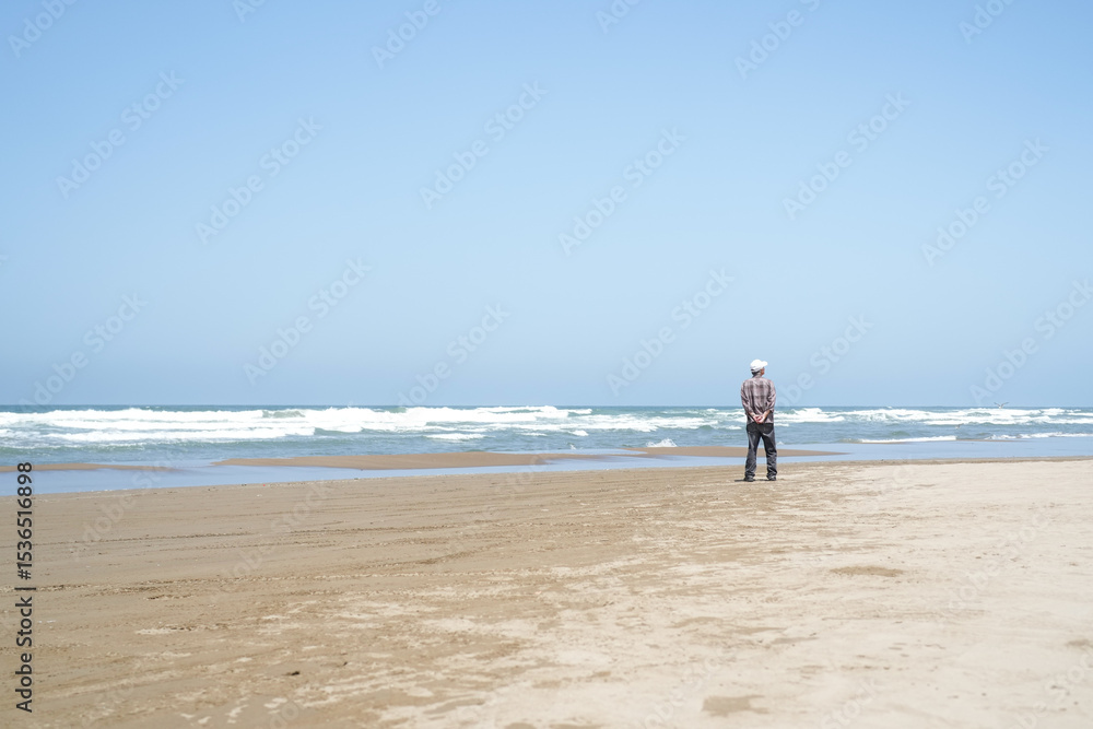 By the rippling Sea of Japan on a sunny May day, a Japanese man in his late 70s wearing a checkered shirt stands alone on the beach. Gentle waves and spring air evoke a quiet moment of reflection. By the rippling Sea of Japan on a sunny May day, a Japanese man in his late 70s wearing a checkered shirt stands alone on the beach. Gentle waves and spring air evoke a quiet moment of reflection.