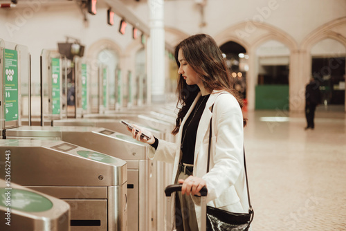 Young woman paying with smartphone via contactless NFC terminal and getting ready for travel at train station in Lisbon. Concept of business travel and individual tourism