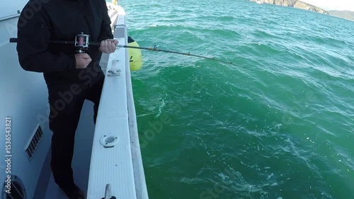 A fisherman pulls a fish out of the water with a fishing rod on a yacht or boat. The boat floats on the water in the sea or ocean.