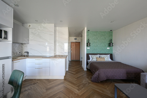 modern studio apartment with a kitchenette and sleeping area. Features a herringbone floor, green wallpaper, and minimalist design