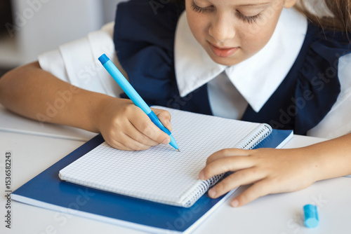 School kig writing a schoolwork in a notebook with a blue pen. Child doing homework.
