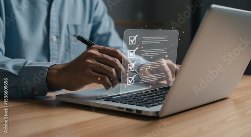 Focused hands check off items on a glowing digital checklist projected onto a laptop screen, completing tasks in a dimly lit workspace