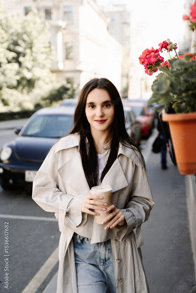 Fototapeta premium Young woman walking with coffee cup on city street in spring