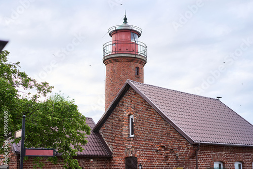 Wallpaper Mural A beautifully picturesque brick lighthouse situated right next to a charming rustic home, all set against a cloudy sky Torontodigital.ca