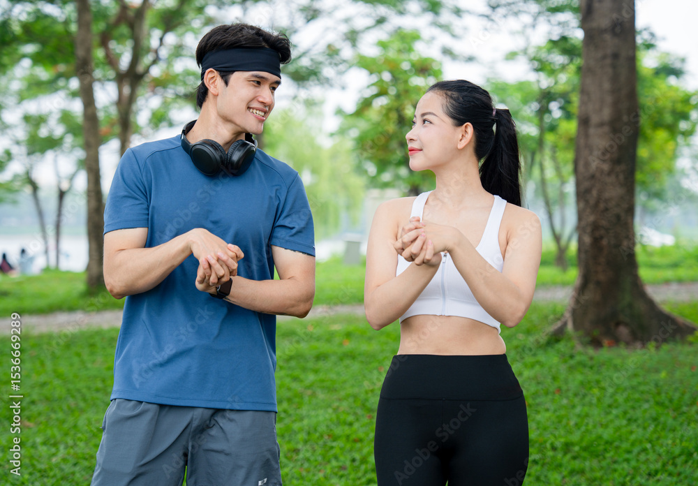 Couple stretching together outdoors on a grassy field with trees in the background They're smiling Couple stretching together outdoors on a grassy field with trees in the background They're smiling