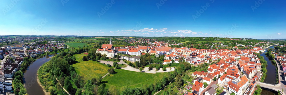 Obraz premium Luftaufnahme von Donauwörth mit roten Dächern, historischen Gebäuden und einem markanten Turm, eingebettet in eine grüne Landschaft. Die Stadt bietet eine charmante Kulisse.