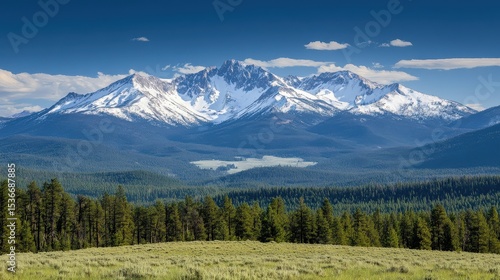 Snowy mountains rise over a forested valley under a blue sky