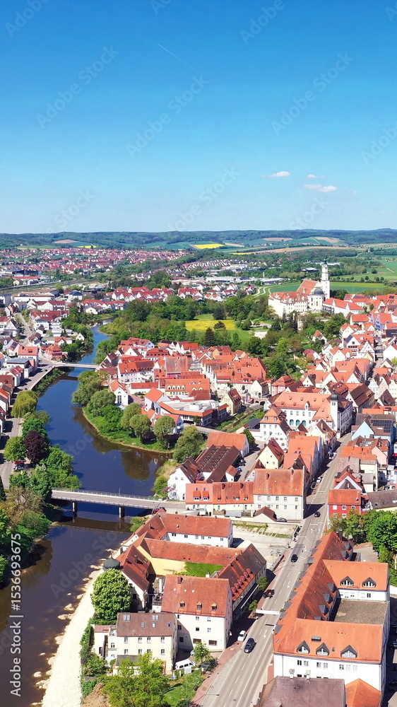 Obraz premium Luftaufnahme von Donauwörth mit roten Dächern, historischen Gebäuden und einem markanten Turm, eingebettet in eine grüne Landschaft. Die Stadt bietet eine charmante Kulisse.