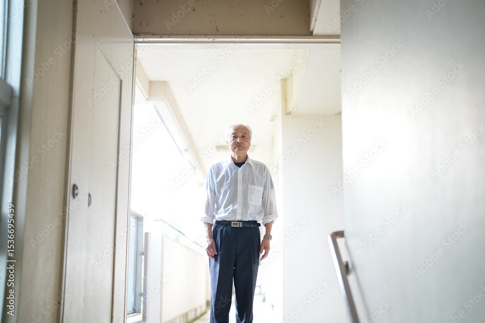 In a Japanese apartment, a Japanese man in his late 70s, wearing a white shirt and white hat, stands by the stairway railing. He gazes ahead in calm silence, lost in thought on a peaceful spring day. In a Japanese apartment, a Japanese man in his late 70s, wearing a white shirt and white hat, stands by the stairway railing. He gazes ahead in calm silence, lost in thought on a peaceful spring day.