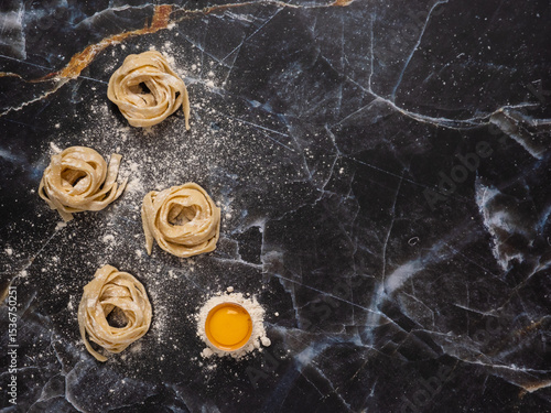 Rolled pasta over a marble surface with a raw egg. Flat lay with a dark background