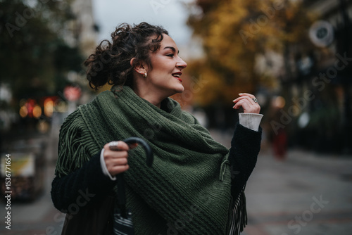 A cheerful woman wearing a green scarf walking outdoors on a brisk autumn day. Her joyful expression and carefree demeanor capture the spirit of enjoying moments during the colorful fall season.