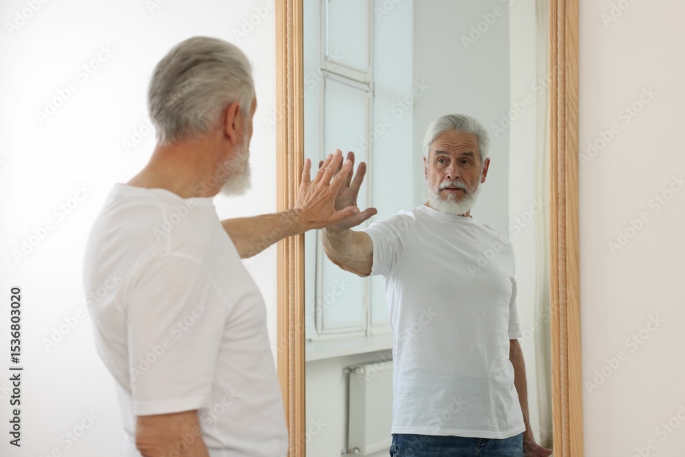 Obraz premium Handsome senior man looking at himself in mirror indoors