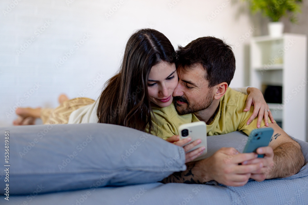 Happy couple lounging together on a cozy bed, enjoying their smartphones while sharing moments of connection and relaxation at home Happy couple lounging together on a cozy bed, enjoying their smartphones while sharing moments of connection and relaxation at home