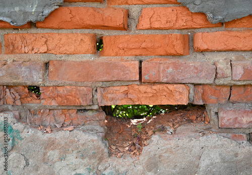 Weathered brick wall showing signs of decay and nature's encroachment through a large gap in the structure