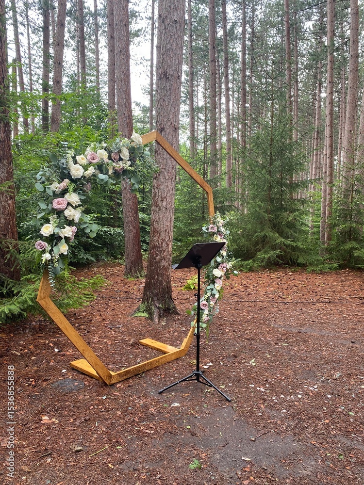 Fototapeta premium Romantic forest wedding altar featuring a hexagon arch adorned with roses and eucalyptus, surrounded by tall pine trees.
