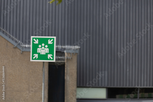 A prominent green emergency assembly point sign, set against a modern building facade, highlighting safety and preparedness.