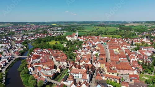 Luftaufnahme von Donauwörth mit roten Dächern, historischen Gebäuden und einem markanten Turm, eingebettet in eine grüne Landschaft. Die Stadt bietet eine charmante Kulisse. 