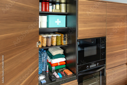 Modern kitchen pantry organized with food and drink supplies, canned goods, non perishable items and clothes. Cupboard stocked for potential emergencies or food scarcity. 72 hours survival kit concept