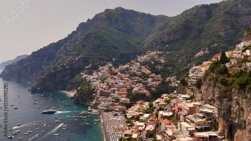 Drone footage of vibrant Positano on Monti Lattari, colorful architecture luxury hotels with blooming plants, descending to turquoise full beach. Private yachts boats sail Salerno Bay, Amalfi