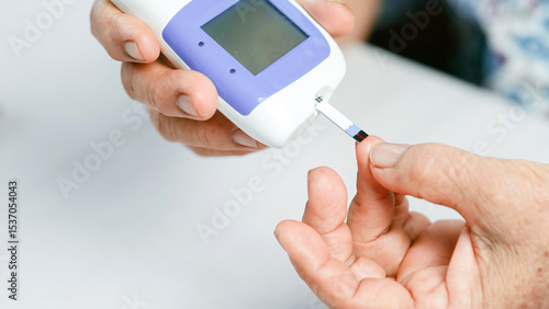 Blood glucose meter diabetes test hand finger medical device healthcare monitoring close up elderly measurement. This close up image shows person using blood glucose meter to check blood sugar